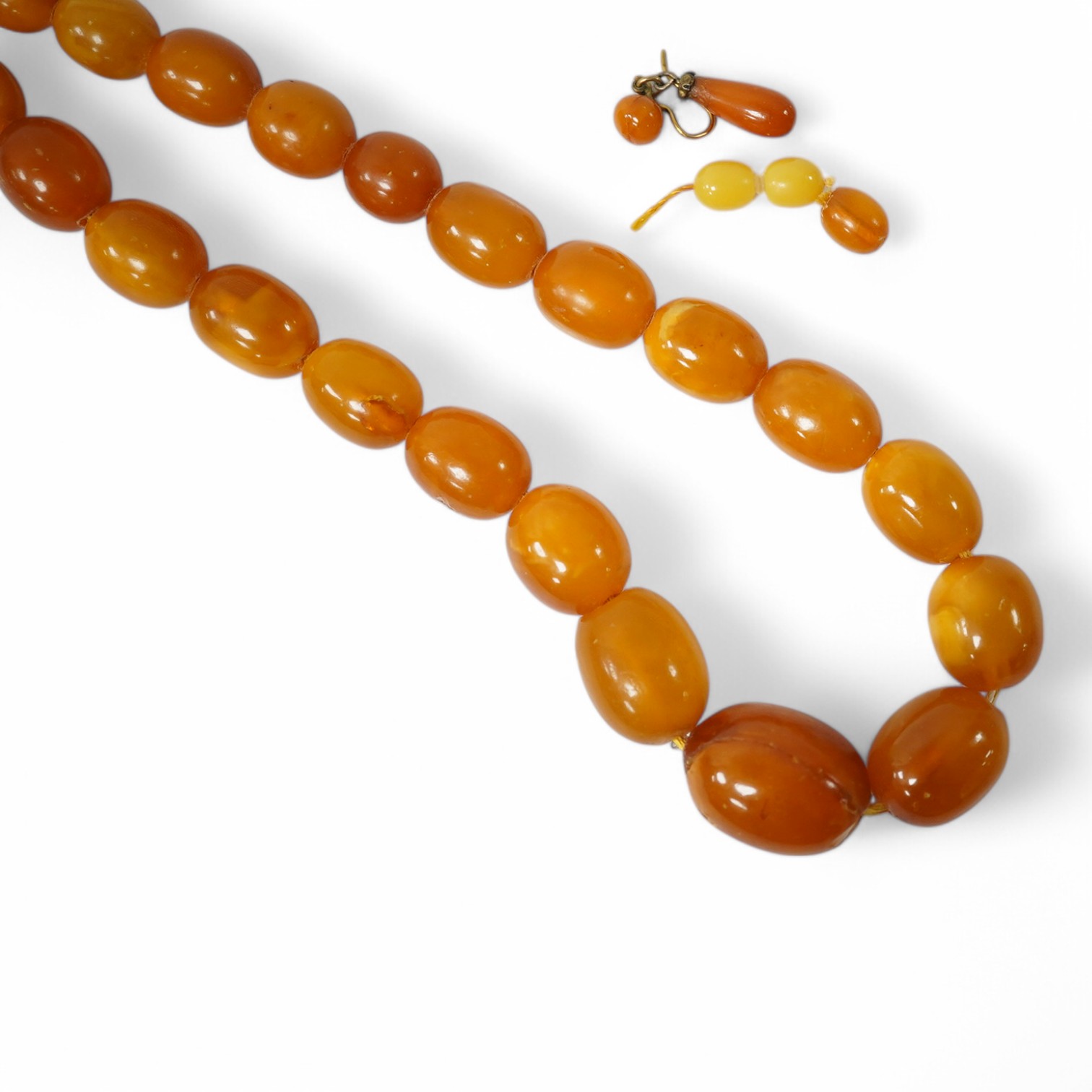 A single strand graduated oval amber bead necklace (a.f.), 90cm, gross weight 72 grams and three odd beads and an earring. Condition - poor